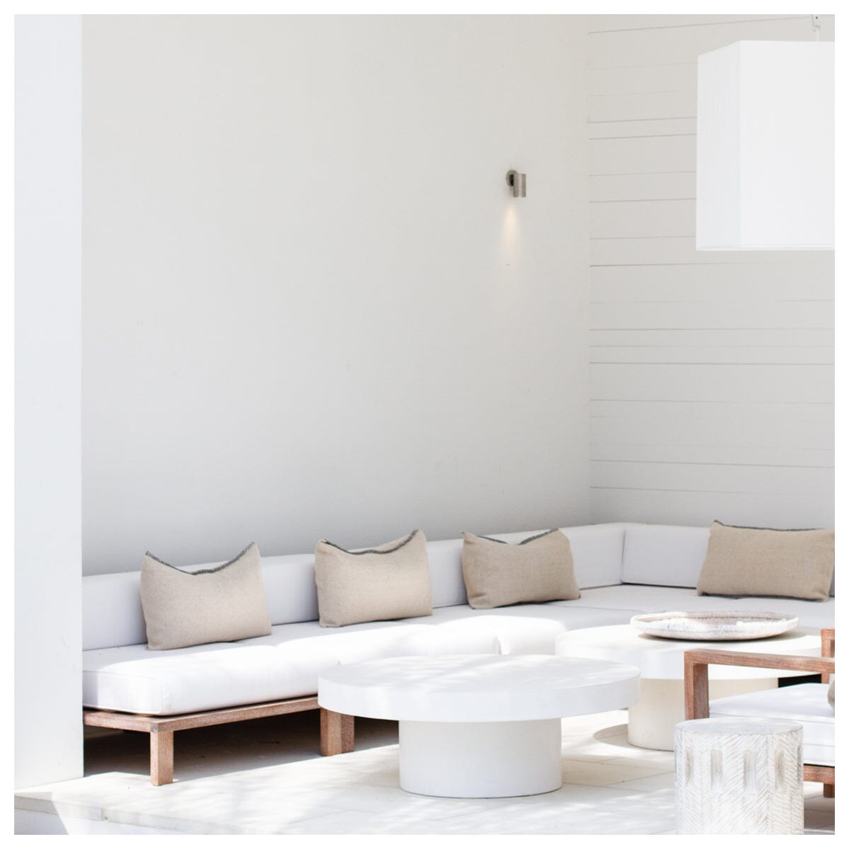 A modular outdoor lounge sectional with a white cushion finish and a natural wood frame, arranged in a spacious indoor setting.