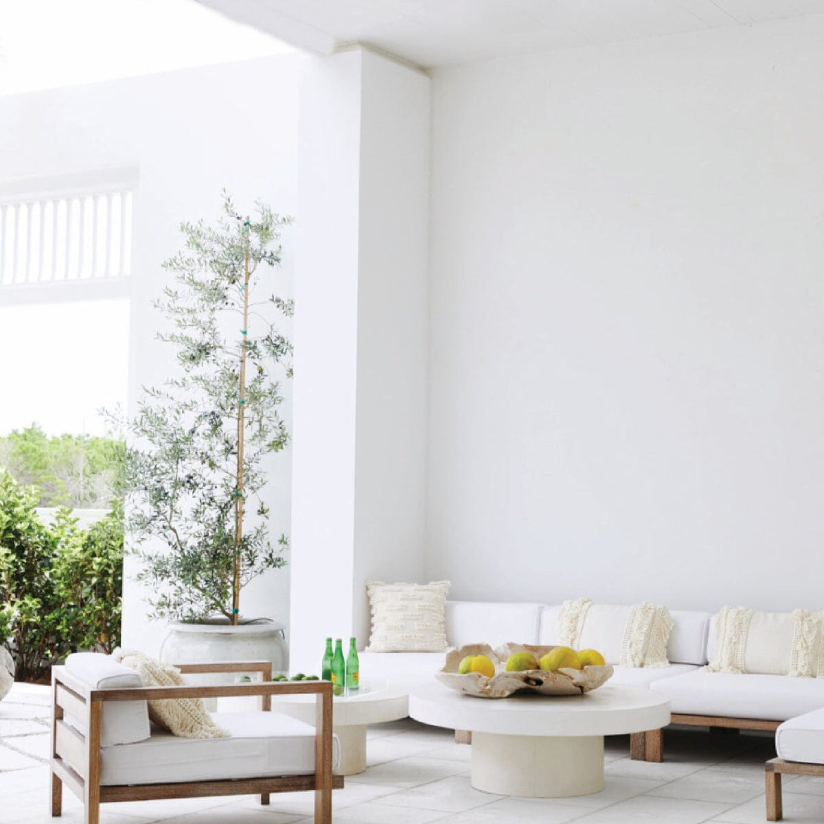 A modular outdoor lounge sectional with a white cushion finish and a natural wood frame, arranged in a spacious indoor setting.