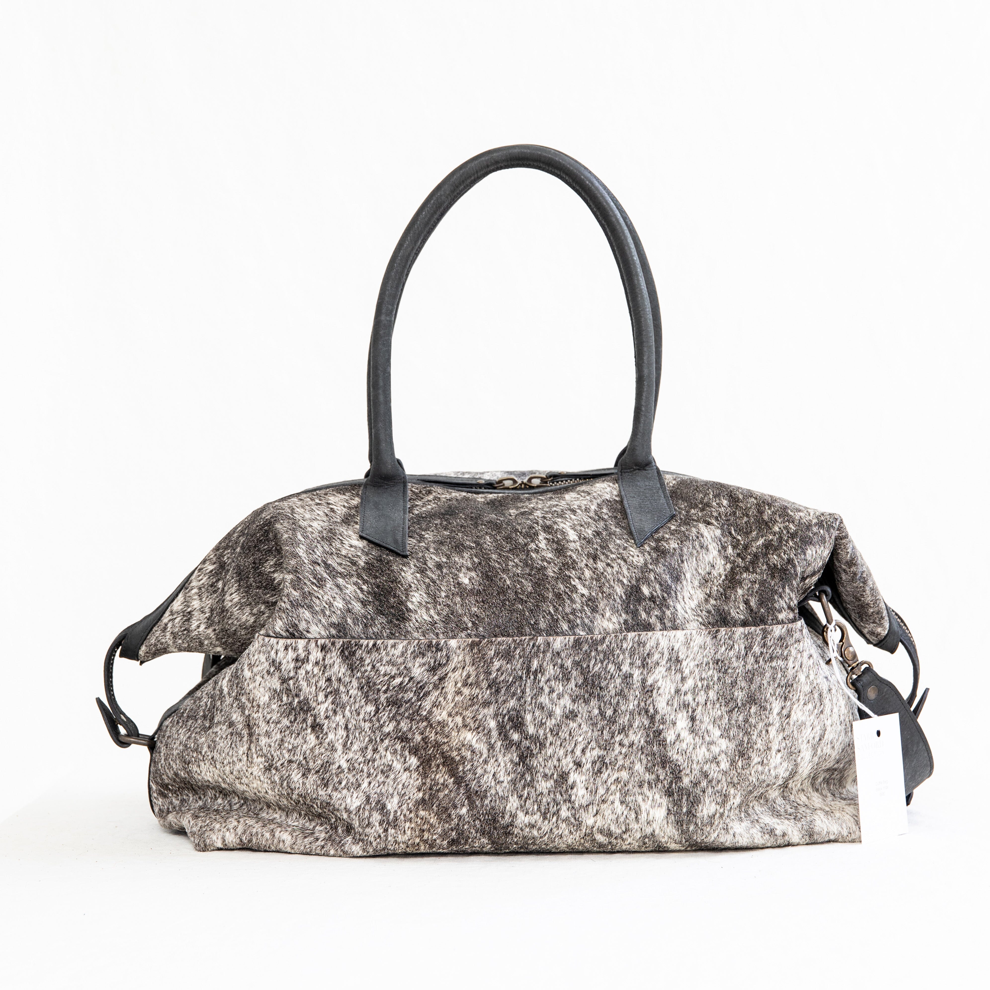 A black leather duffle bag with a hair-on-hide texture, featuring two handles and an adjustable shoulder strap, displayed against a white background