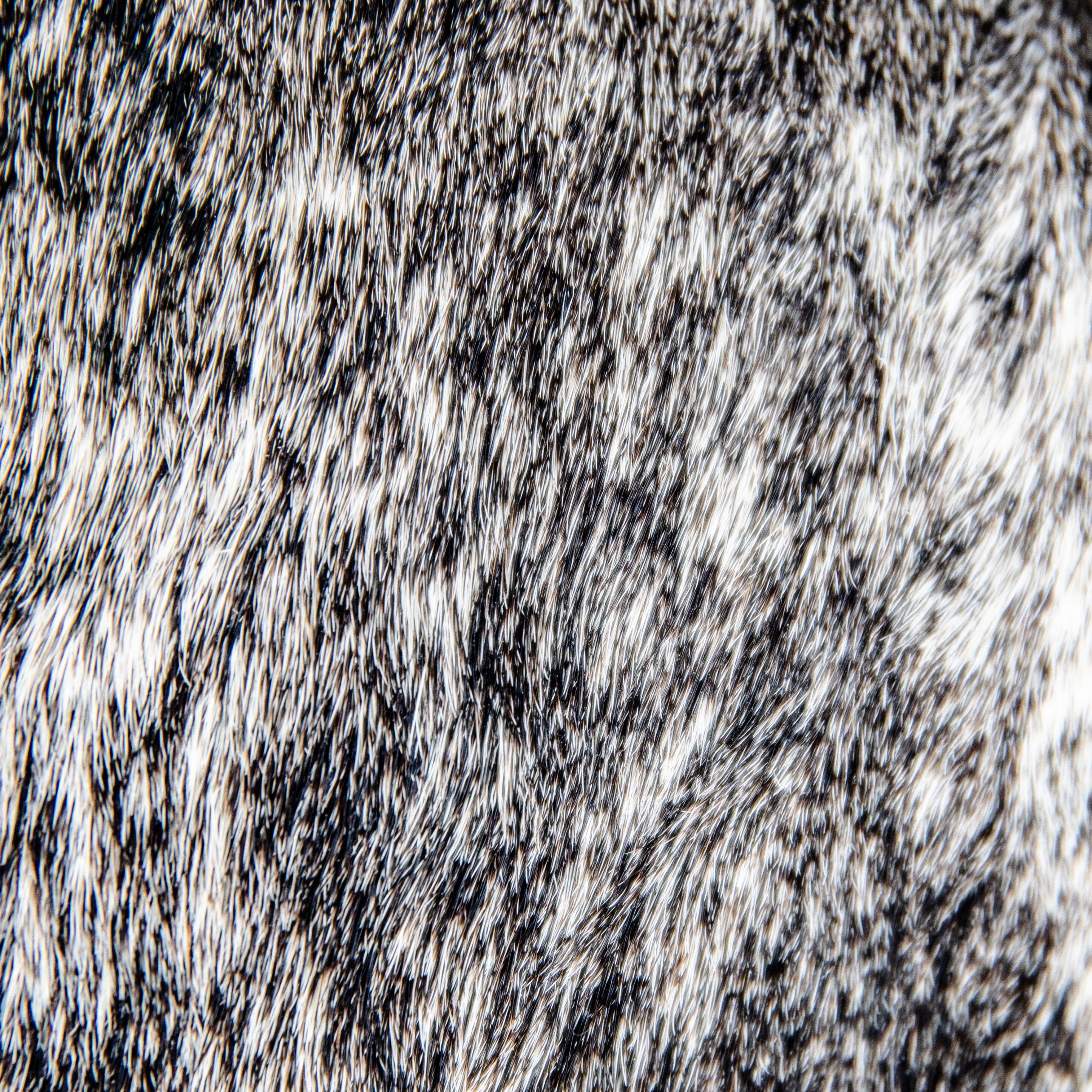 A black leather duffle bag with a hair-on-hide texture, featuring two handles and an adjustable shoulder strap, displayed against a white background