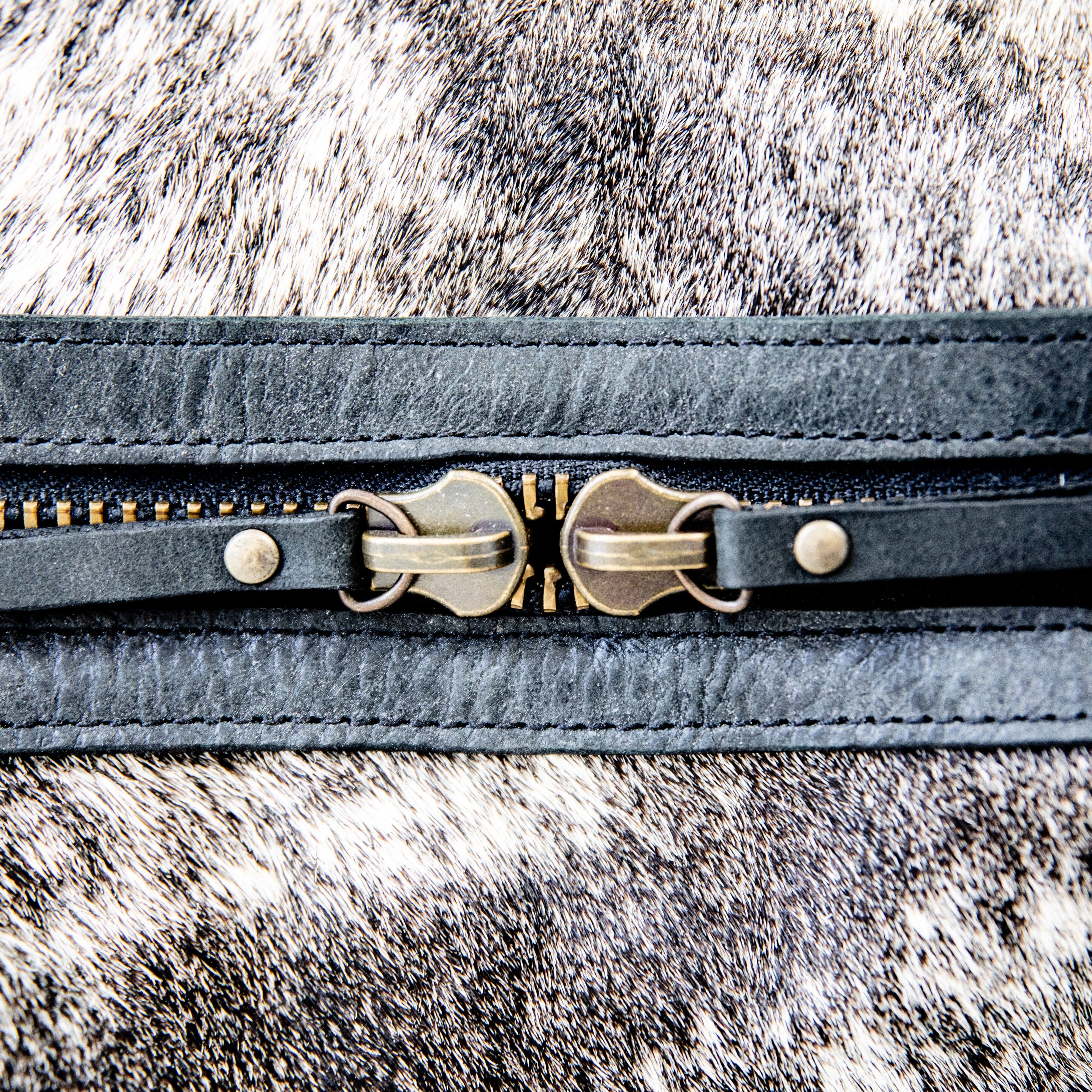 A black leather duffle bag with a hair-on-hide texture, featuring two handles and an adjustable shoulder strap, displayed against a white background