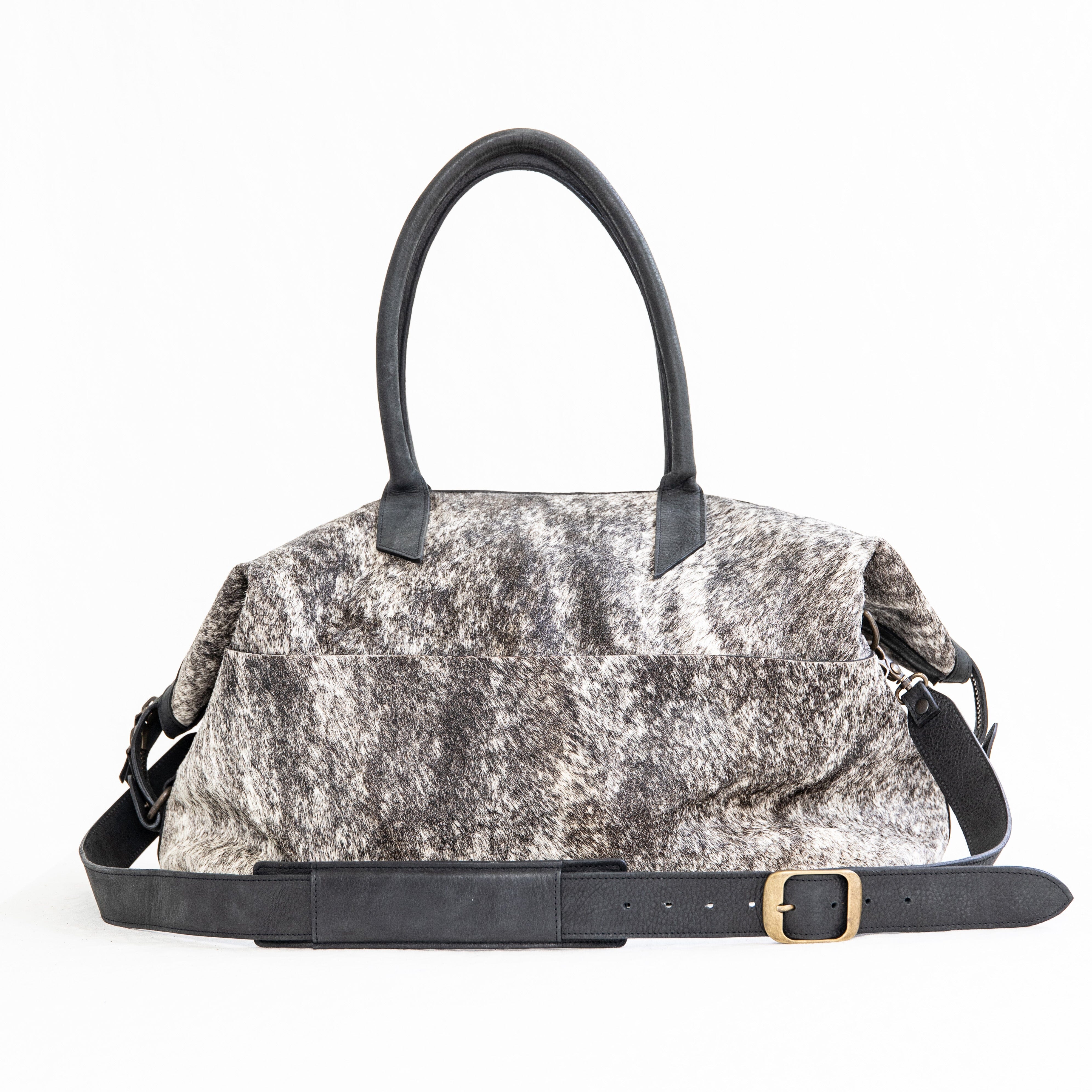 A black leather duffle bag with a hair-on-hide texture, featuring two handles and an adjustable shoulder strap, displayed against a white background