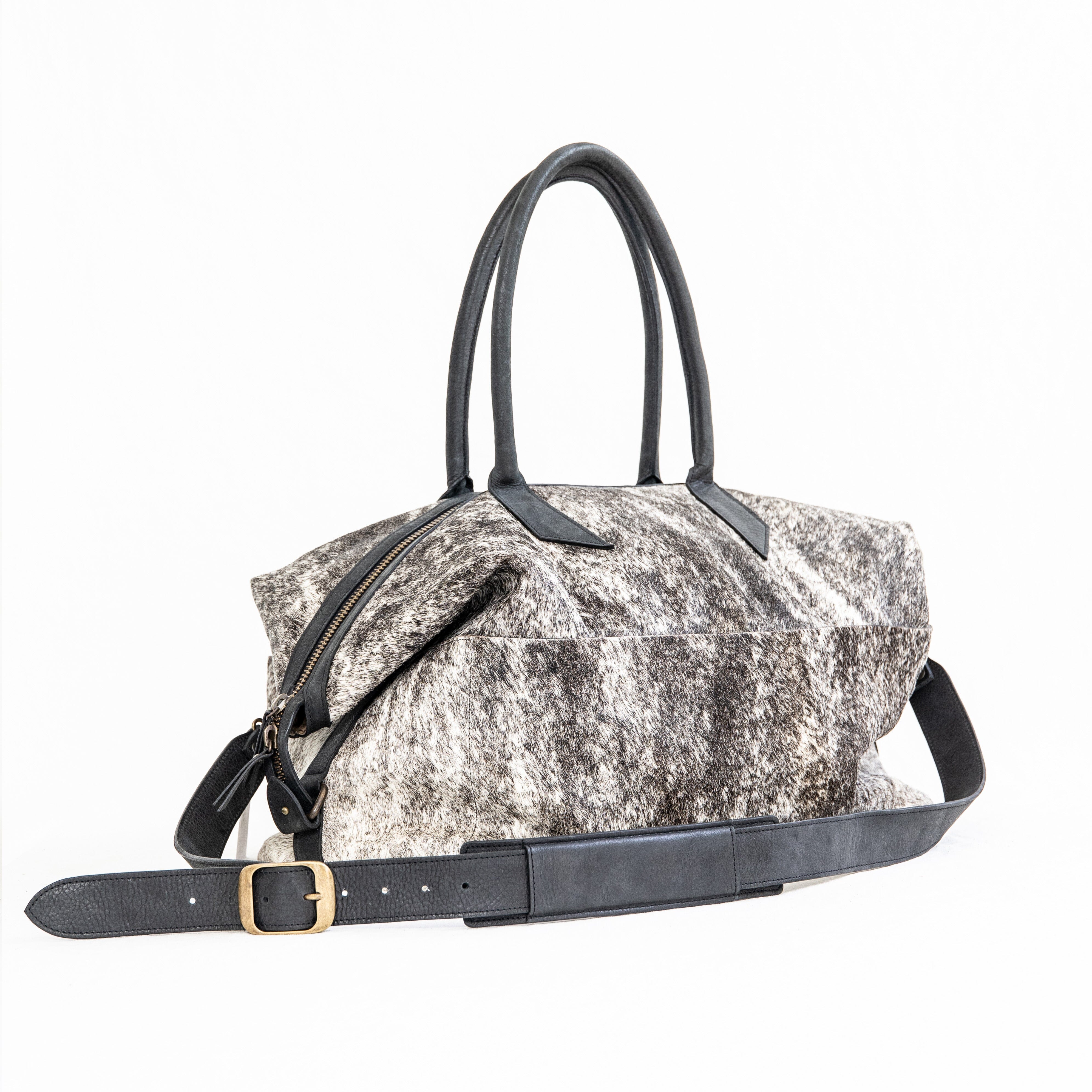 A black leather duffle bag with a hair-on-hide texture, featuring two handles and an adjustable shoulder strap, displayed against a white background