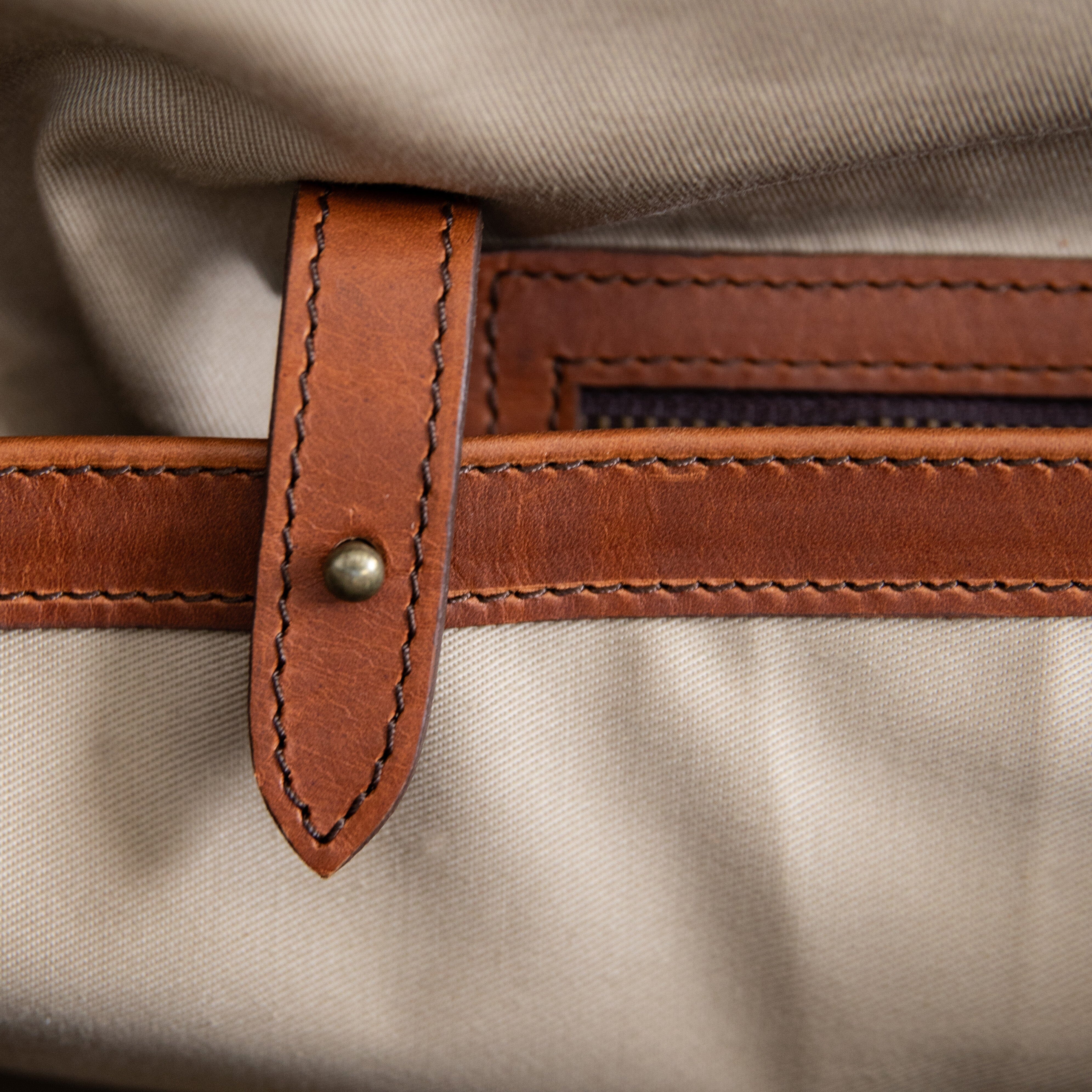 A brown duffle bag with a hair-on-hide design, featuring a leather handle and shoulder strap, brass clasps, and zipper enclosures.