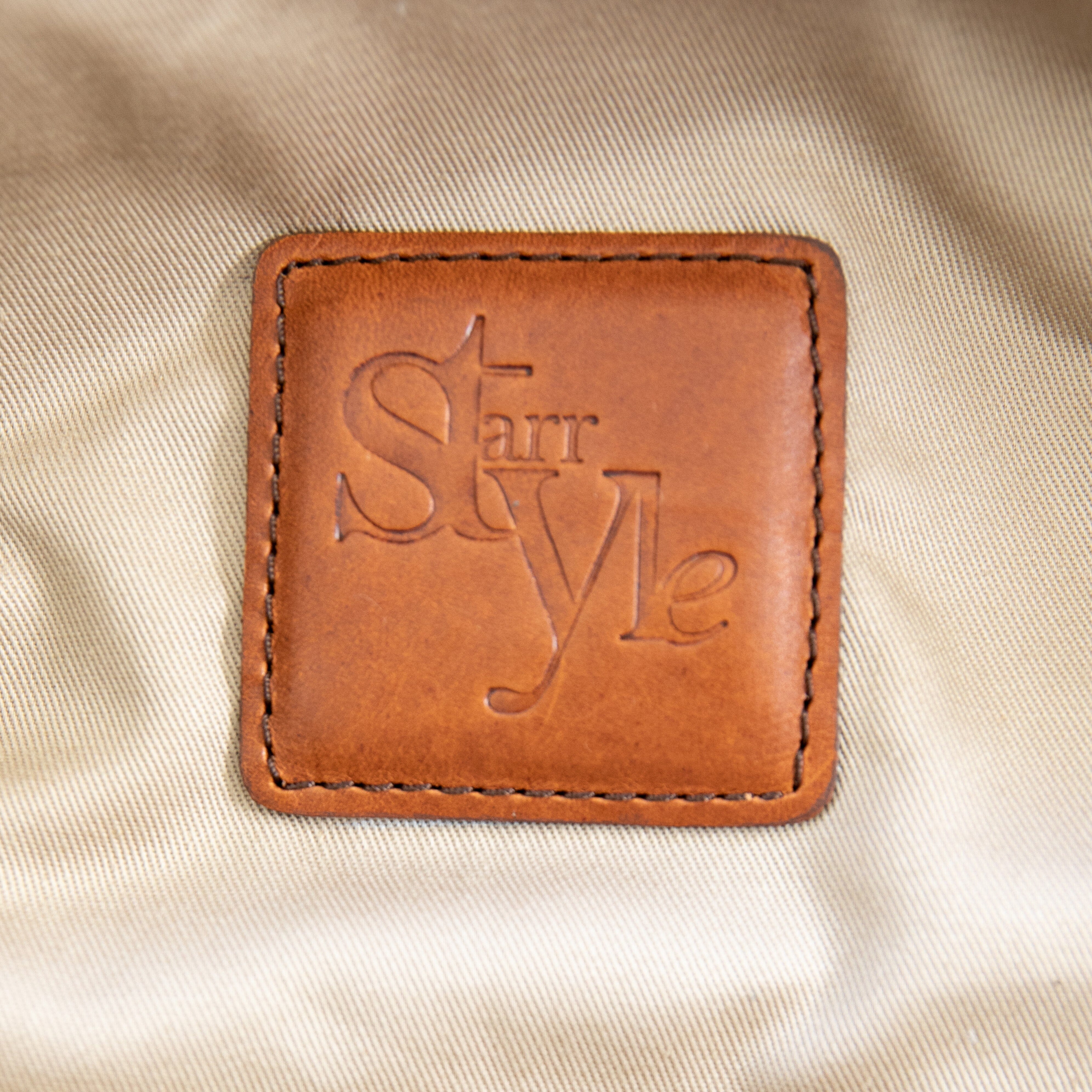 A brown duffle bag with a hair-on-hide design, featuring a leather handle and shoulder strap, brass clasps, and zipper enclosures.