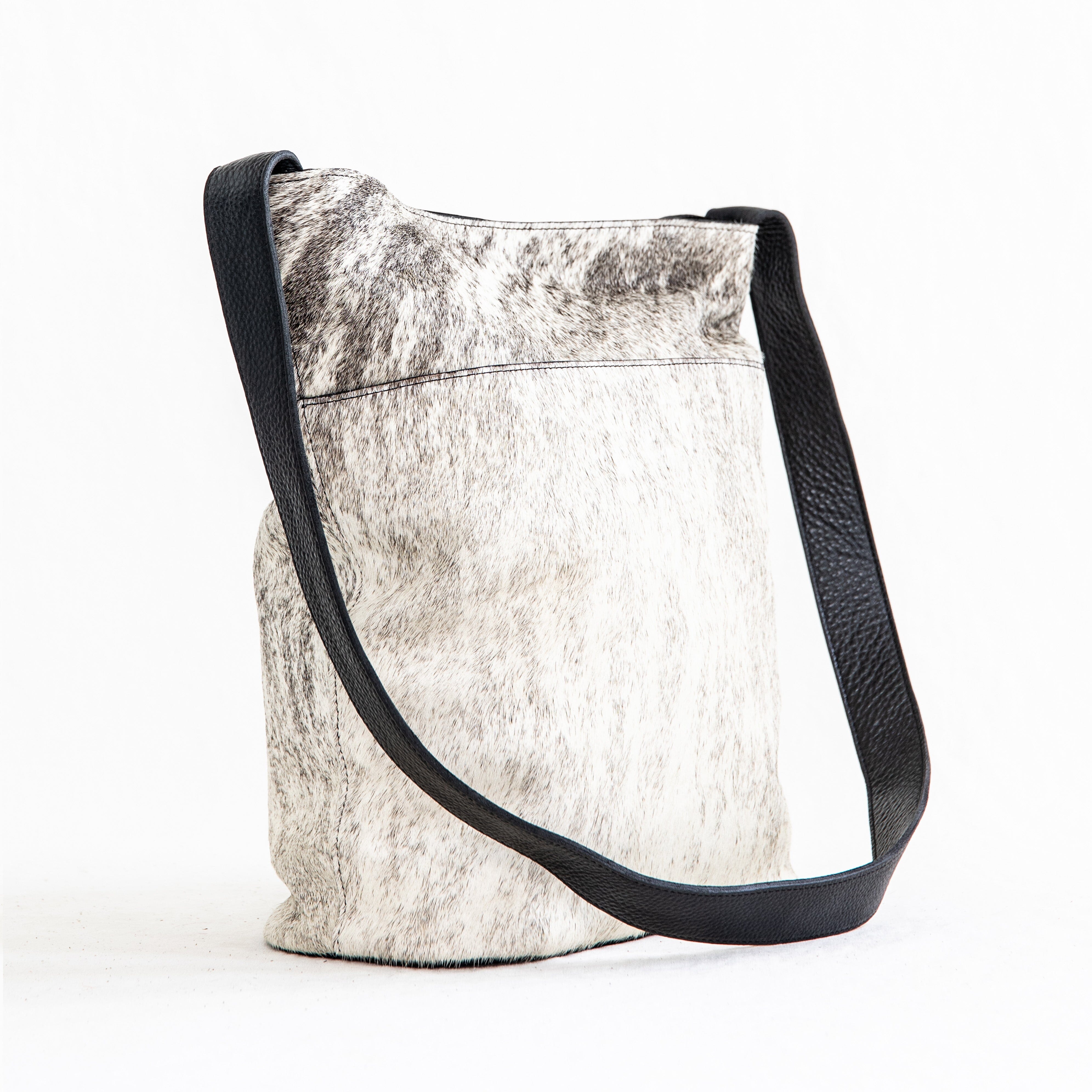 A white and beige crossbody shoulder bag made of hair-on-hide leather, featuring a brass clasp and a black shoulder strap.