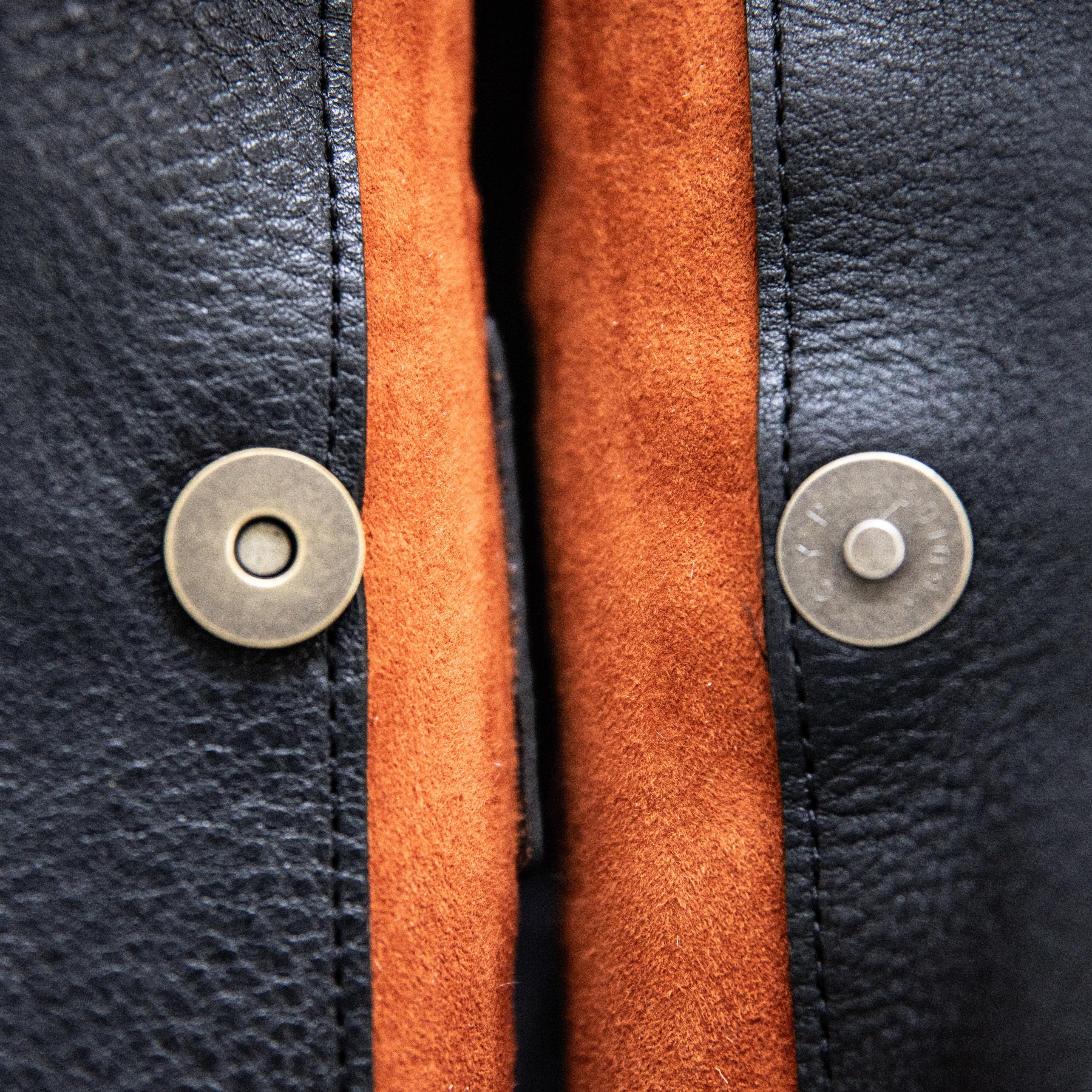 A white and beige crossbody shoulder bag made of hair-on-hide leather, featuring a brass clasp and a black shoulder strap.