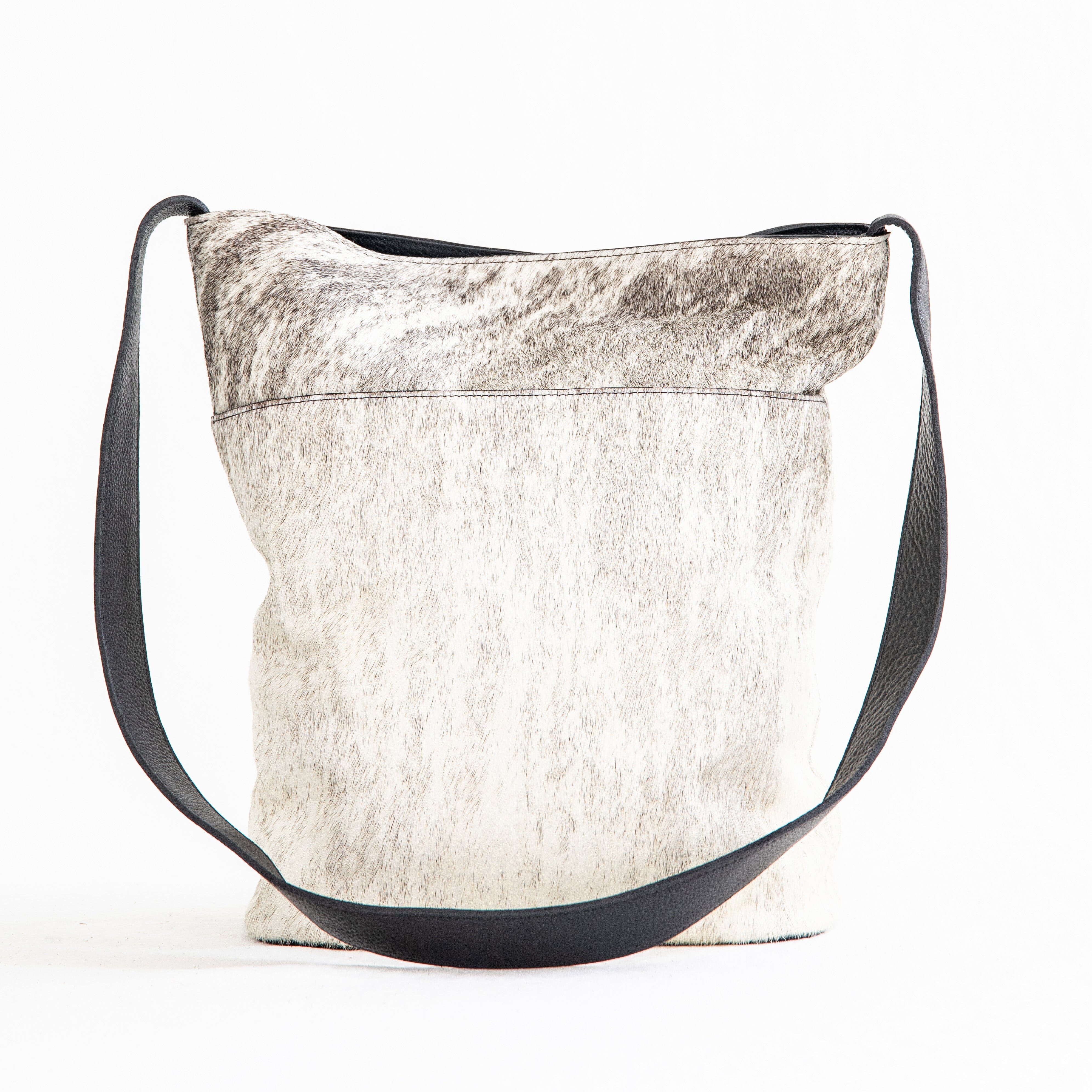 A white and beige crossbody shoulder bag made of hair-on-hide leather, featuring a brass clasp and a black shoulder strap.